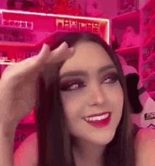 a woman is smiling and holding her hand to her forehead in front of a pink shelf .