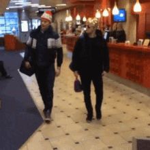 a man wearing a santa hat walks with a woman in a lobby