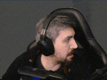 a man with a beard wearing headphones is sitting in a gaming chair .
