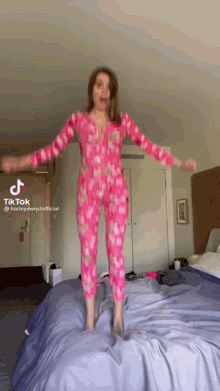a woman in pink pajamas is jumping on a bed ..