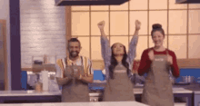 a group of people are standing in a kitchen with their hands in the air .