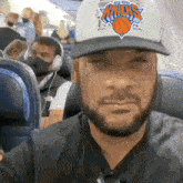 a man wearing a new york knicks hat sits on a plane