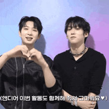 two young men are making a heart shape with their hands while standing next to each other
