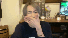 a person covering their mouth with their hand in front of a sign that says shots