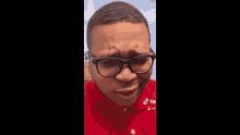 a man wearing glasses and a red shirt is making a sad face .