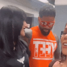 a man with a beard wearing sunglasses and an orange shirt with the word teey on it