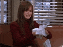 a woman in a red sweater is sitting on a couch holding a pile of crumpled paper .