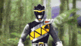 a black and yellow power ranger stands in a forest