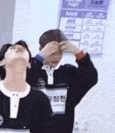 a couple of men are standing next to each other and one of them is covering his eyes with his hands .