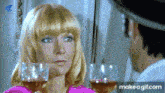 a woman in a pink shirt is looking at a man in a white hat while holding two wine glasses
