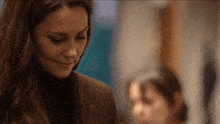 a woman in a brown suit and black turtleneck is smiling while looking down .