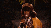 a man wearing a fur hat and a varsity jacket is singing into a microphone ..