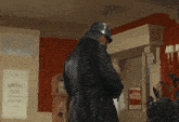a man in a black coat and helmet is standing in a room