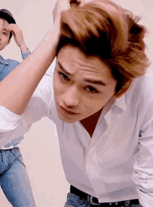 a man in a white shirt is holding his hair while another man looks on .