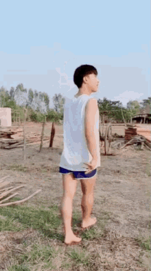 a young man in a white tank top and blue shorts is standing on a grassy field .