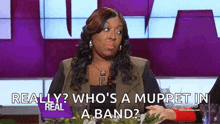a woman is sitting at a table with a muppet in a band on her face .