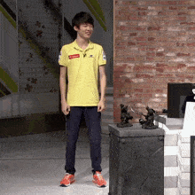 a young man wearing a yellow shirt that says supreme is standing in front of a brick wall