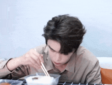 a young man is eating food with chopsticks .