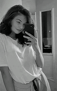 a woman is taking a selfie in front of a mirror with her cell phone .