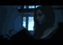 a woman is reading a book in a dark room with a window in the background