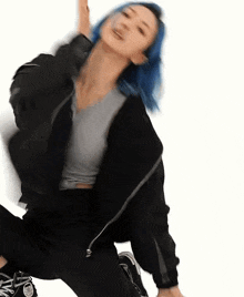 a woman with blue hair is wearing a black jacket and black pants and is dancing .