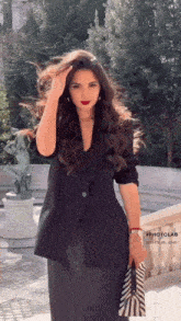 a woman in a black suit is holding a purse