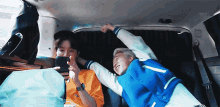two men are laying in the back of a car playing a game on a cell phone .