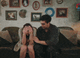 a man and a woman sit on a couch with pictures on the wall behind them