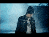 a man is standing in the rain wearing a hat and a jacket .