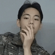 a man in a military uniform is covering his mouth with his finger .