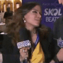 a woman with a microphone in front of a sign that says skol beat