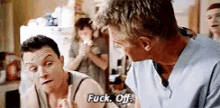 a man in a blue scrub top is talking to another man in a kitchen and saying `` fuck off '' .