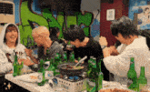 a group of people are sitting at a table with bottles of beer and food