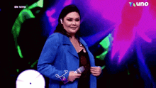 a woman in a blue jacket is holding a microphone in front of a purple background that says en vivo on it