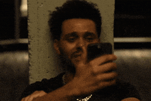 a man leans against a wall while looking at his phone