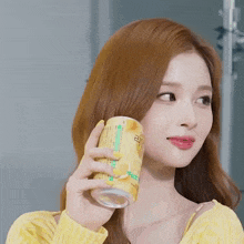 a woman in a yellow shirt is holding a can of soda in her hand .