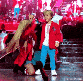 a little boy in a red jacket is standing next to a woman in a red jacket on a stage ..