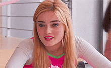 a young woman with blonde hair is wearing a pink and green top and a white shirt .