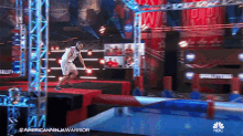 a man in a basketball uniform is jumping over a water obstacle in an american ninja warrior show