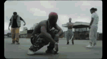 a group of men are standing around a man kneeling down in a parking lot .