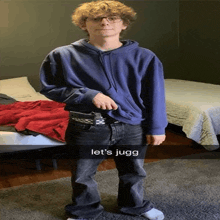 a young man wearing a blue hoodie and black jeans is standing in a bedroom holding a gun .