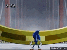 sonic the hedgehog is standing in front of a gold ring on a stage .