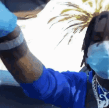 a man wearing a blue shirt and a mask is holding his arm up in the air .