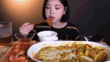 a woman is eating a plate of food with chopsticks and a glass of beer in the background