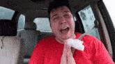 a man in a red shirt is blowing his nose with a tissue