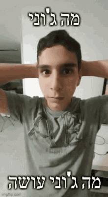 a young man is covering his ears with his hands while wearing a gray shirt with hebrew writing on it .