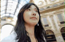 a woman with long black hair stands in front of a building with arches