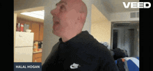 a bald man wearing a black nike shirt stands in front of a white refrigerator