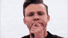 a young man is covering his mouth with his hand while looking at the camera .