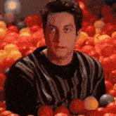 a man in a striped shirt is sitting in a ball pit filled with tomatoes